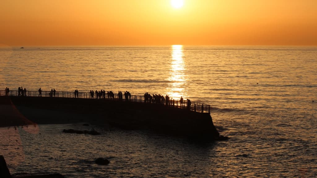 silhouettes of people on a pier at sunset over the sea