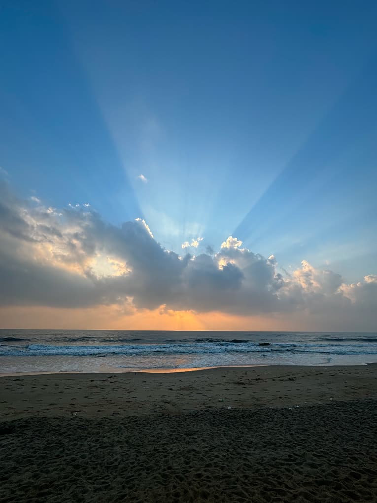 sun rays breaking through clouds over a beach at sunset