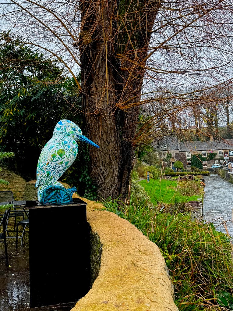 a mosaic kingfisher sculpture on a wall beside a river
