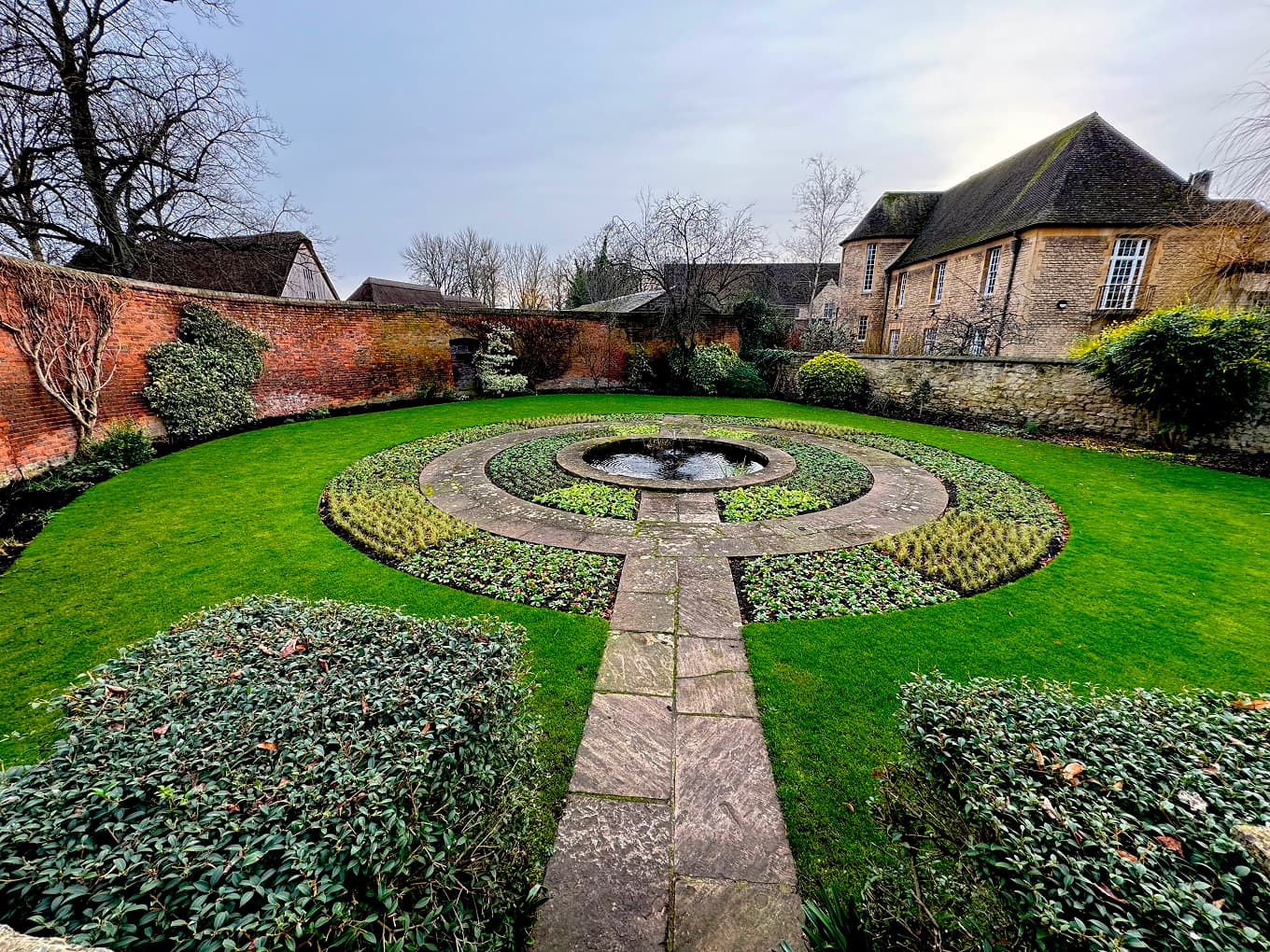 a circular formal garden with a central fountain in front of a stone house