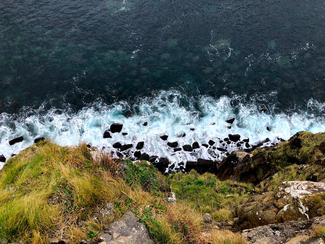 waves breaking on a rocky headland, seen from a cliff top